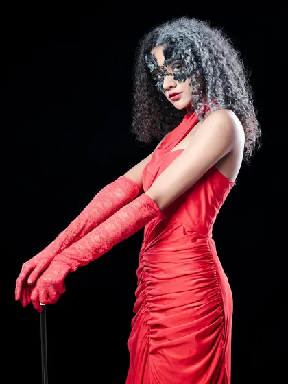 The original studio shot for the 'Cruella' theme, showing the model in a red dress and mask against a clean black background before the creative edit.