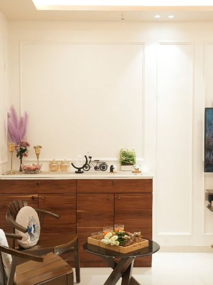 We designed this custom wooden crockery unit to provide storage while adding warmth to the white-themed living room. The classic wooden chairs create a charming corner for conversations.