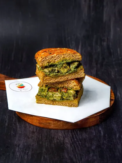 A stacked sandwich with a green pesto filling, shot against a dark, dramatic background. This vertical composition and moody lighting make the sandwich look substantial and delicious.