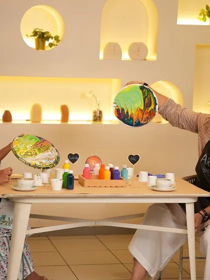 Sucharita and Ali engaged in the fluid art process, pouring and tilting their canvases to create their designs. It's a very intuitive and playful form of art.