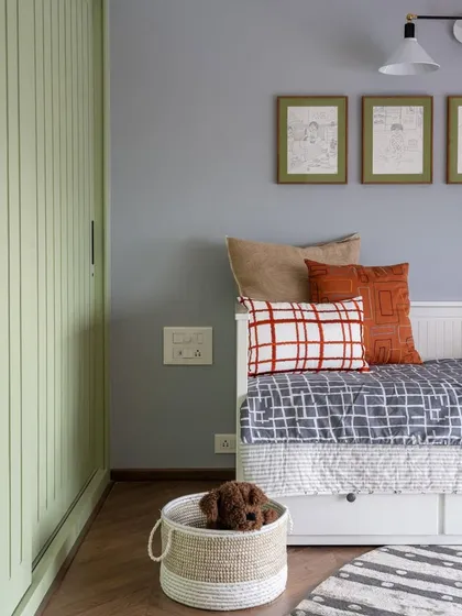 This cozy bedroom corner in the 'Inde Blue' project features a daybed layered with textured pillows and throws. The soft, muted color palette and simple, framed sketches on the wall create a calm and personal space for rest.