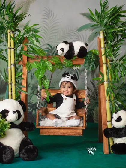 Surrounded by his panda friends, this little one is having a beary good time on a wooden swing in our jungle-themed studio.