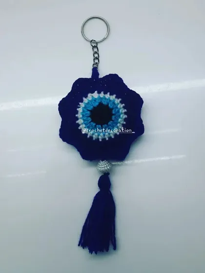 This is our flower-shaped evil eye or nazar battu keychain, designed to bring good vibes. Made with deep blue yarn and finished with a tassel, it's a beautiful and meaningful charm for your keys or to hang in your car.