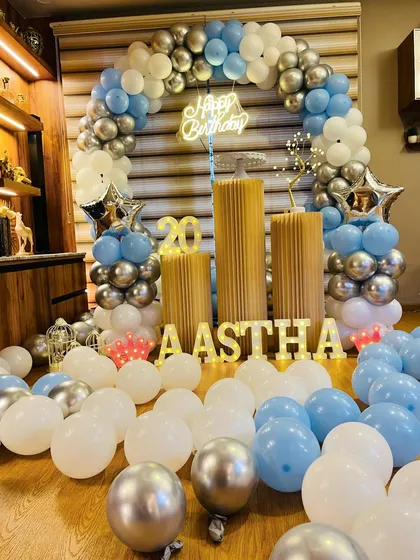 A cool and stylish birthday setup for a 20th birthday. The balloon arch in pastel blue, white, and chrome silver creates a chic look, complemented by marquee letters and numbers.
