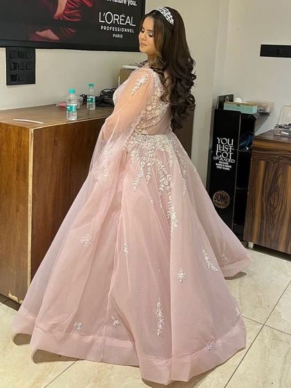 A side profile of a lovely pastel pink gown with delicate white embroidery and flowing sheer sleeves. This rental is perfect for achieving a soft, romantic look for your engagement or reception.