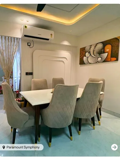 A modern dining setup with quilted beige chairs and a simple, elegant table. The Ganesha art piece adds a spiritual and artistic touch to the space.