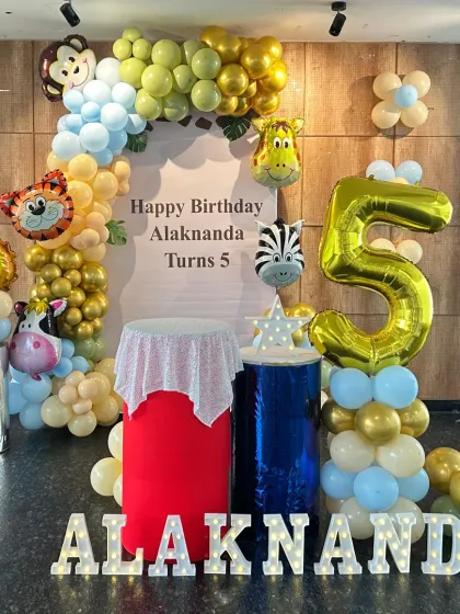 A fun jungle animal-themed 5th birthday party. The decor features an arch of pastel blue and yellow balloons adorned with foil animal heads like a lion, tiger, and zebra.