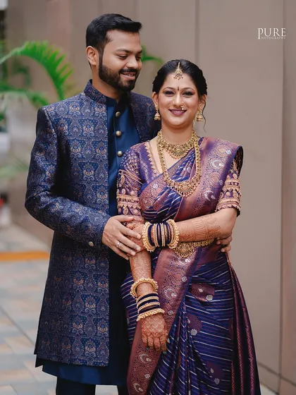 A classic portrait of the couple in their stunning reception outfits. The bride's purple Paithani saree and the groom's patterned bandhgala are showcased perfectly.