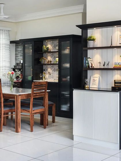 This monochromatic dining room uses a black and white palette for a chic and timeless look. The bar unit features fluted white panels, while the black crockery cabinet has patterned wallpaper inside for a touch of detail.