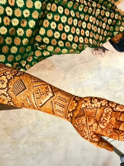 A single-arm view of a detailed bridal session in progress. You can see the groom's name, 'SHIV', artfully integrated into the design on the palm.