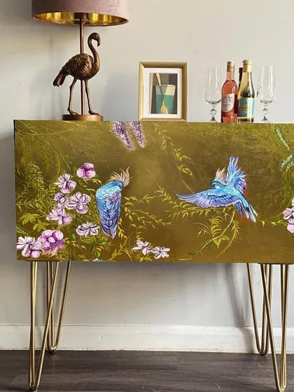 I transformed this bar unit with a shimmering gold leaf finish and delicately drawn birds and leaves for a vintage ambiance. It's a unique style that adds a captivating charm to the space.