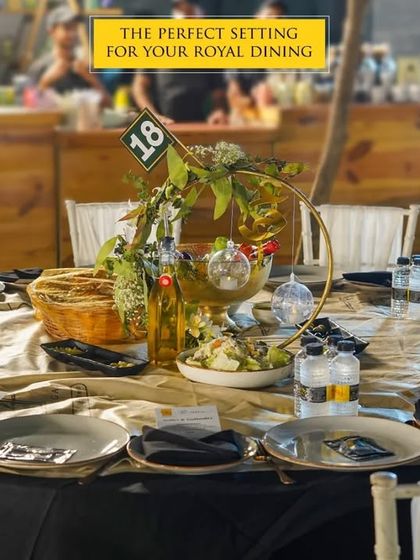 The perfect setting for your royal dining experience. This table is set with dark, elegant tableware and a beautiful centerpiece, creating a sophisticated and intimate atmosphere for guests at an evening event.
