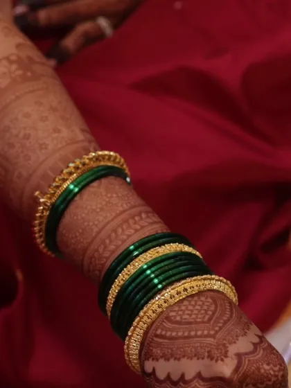 A close-up showing the deep maroon stain of the mehndi against the client's skin and her green bangles.