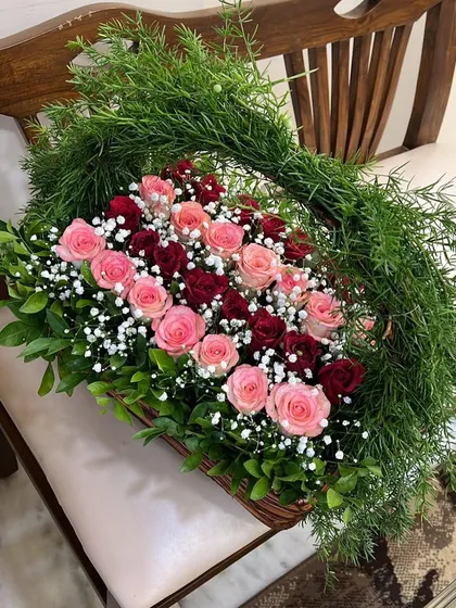 Happiness is fresh flowers in a basket! This stunning arrangement features a gradient of red and pink roses, surrounded by lush greenery and a dramatic, leafy handle.