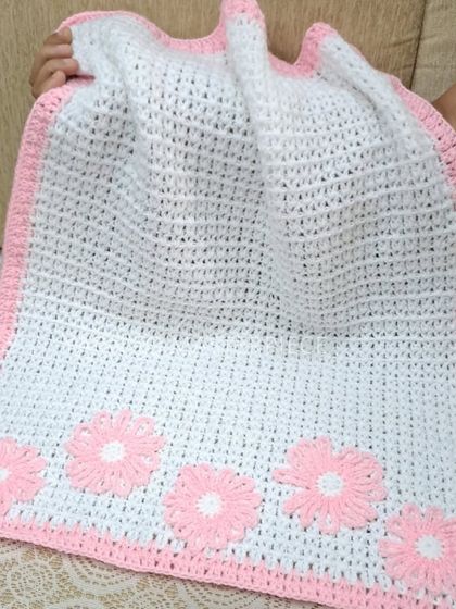 A handmade baby blanket in white with a delicate pink border and matching flower appliqués. It's soft, warm, and perfect for a baby's crib or stroller.