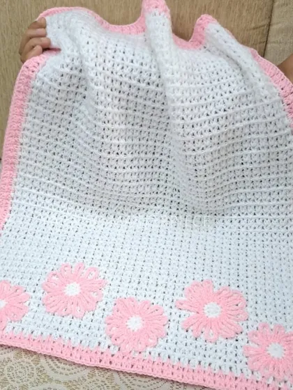 A classic color combination, this baby blanket is white with a soft pink border and features five matching pink daisy flowers.