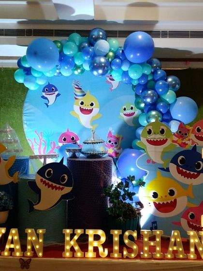 A fun Baby Shark themed setup with character cutouts swimming around the cake table and a blue balloon garland representing the ocean.