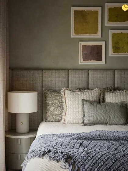 A close-up of the guest bedroom's styling. The combination of different pillow textures, a knitted throw, and abstract art against a textured wall showcases our attention to detail in creating layered, tactile interiors.