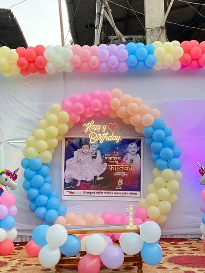 A unicorn-themed birthday stage with a rainbow pastel balloon arch and unicorn sculptures.
