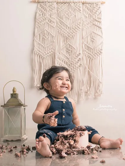 The aftermath of a successful cake smash. This little one's joyful, messy face in a boho-themed setup is a picture of pure delight.