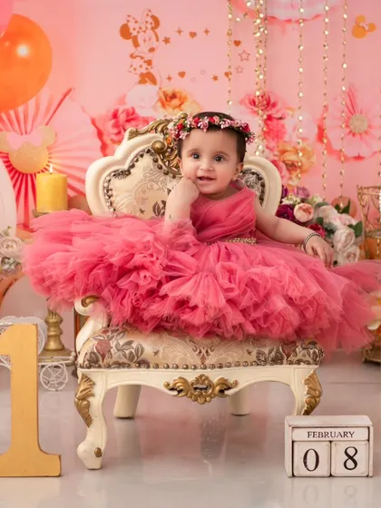 A royal first birthday portrait. The ornate chair, pink tulle dress, and floral crown make this little girl look like a true princess on her special day.