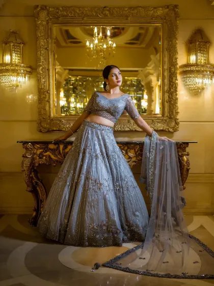 A full-length bridal portrait in a luxurious, golden-lit hall. The bride's pose is confident and graceful, and her beautiful lehenga spreads out around her, creating a truly magnificent image.