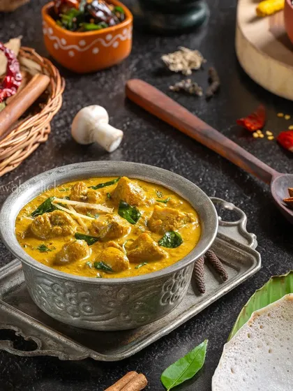 Chettinad Kalan Masala, a spicy mushroom curry. The image is styled with a variety of whole spices to suggest its complex flavors.
