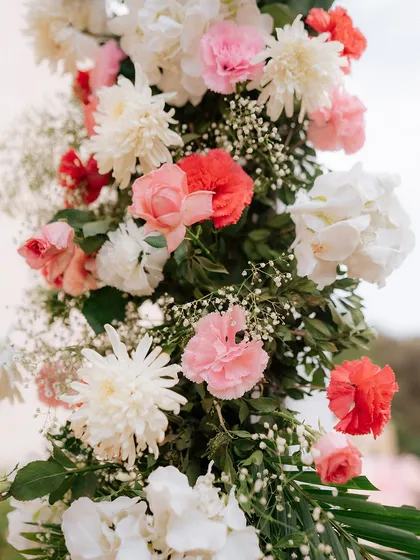 A close-up showcasing the beauty and freshness of our floral arrangements. This pillar is adorned with a mix of pink and red carnations, white chrysanthemums, and delicate baby's breath.