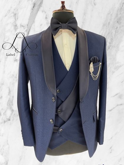 A classic navy blue three-piece tuxedo with a contrasting black shawl collar. This is a timeless look, perfectly tailored to create a sharp and elegant silhouette for any formal occasion.