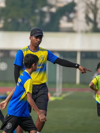 A coach points and gives direct instructions to a player on the field. This image reflects our coaching style: telling players what they need to hear so they can become the best version of themselves.