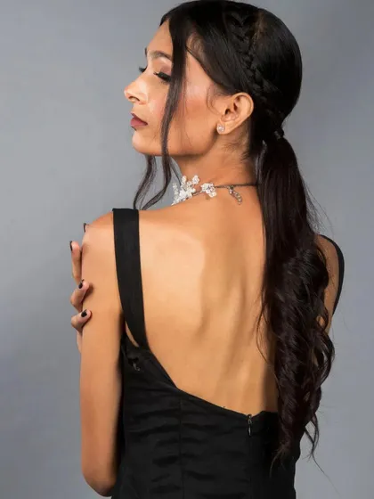 A side profile that beautifully displays the intricate braided ponytail and the delicate line of the model's back. This type of shot is excellent for highlighting hair and makeup artistry within a fashion context.