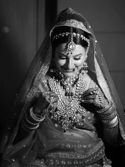 A stunning black and white close-up of the bride. This shot highlights the incredible detail of her jewelry and the happy, gentle expression on her face as she gets ready.