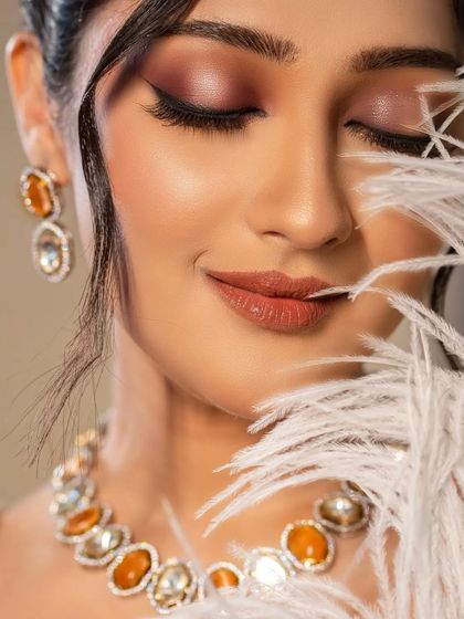 An artistic close-up of the bride, using a white feather to add a soft, ethereal texture to the portrait. This highlights her serene expression and makeup.