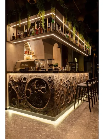 This unique bar counter features a sculptural, textured front resembling a lunar surface, complemented by warm under-counter lighting. The design is bold and artistic, creating a memorable centerpiece for the cafe.