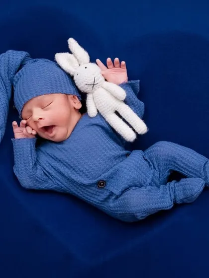 A yawning newborn in a blue outfit, cuddling a crochet bunny inside a heart-shaped prop. Capturing these real moments is key.