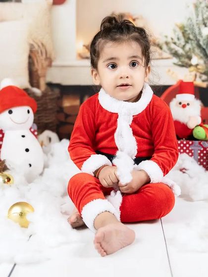 A sweet portrait of a toddler girl in her Santa outfit, sitting amidst a snowy, festive scene.