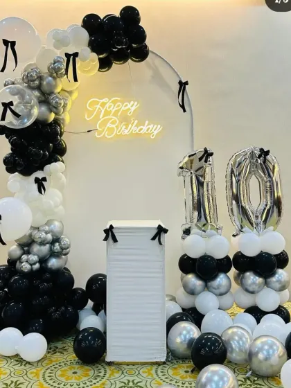 A chic black, white, and silver theme for a 10th birthday, featuring a minimalist arch, a neon sign, and balloon columns with foil numbers.