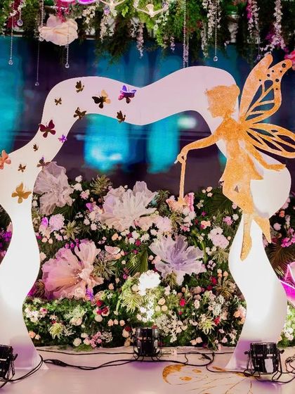 A stunning entrance arch for an enchanted garden party. A custom-sculpted fairy and butterfly archway welcomes guests into a world of magic, set against a backdrop of lush flowers and glowing butterflies.