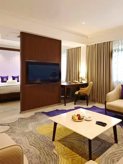 A spacious suite at Vivanta Bengaluru, with a partition separating the living and sleeping areas. The design uses a vibrant rug and purple accents to create a lively yet sophisticated atmosphere.