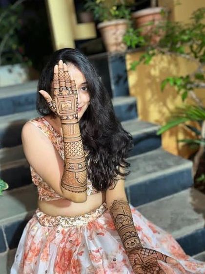 A happy client posing with her festive mehndi, featuring a personalized design on her palm.