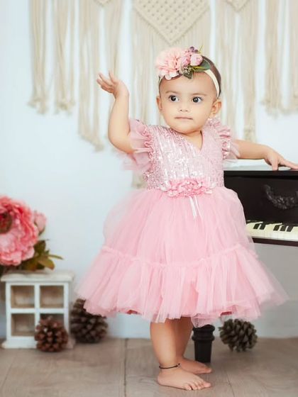 A little princess celebrating her first birthday. She's standing by our mini piano in a beautiful pink dress, ready for her party.