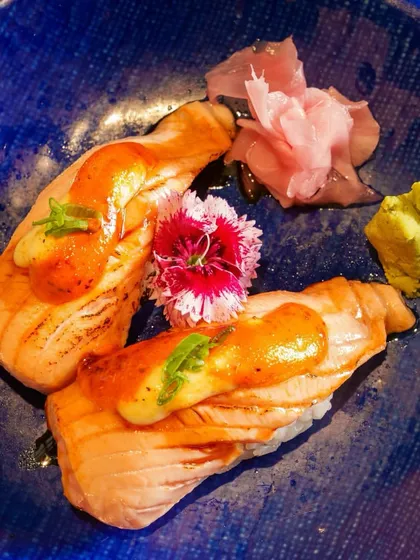 Perfectly crafted Aburi Salmon Nigiri, where torched fish meets seasoned rice. The vibrant blue plate makes the colors of the dish pop, inviting you to indulge.