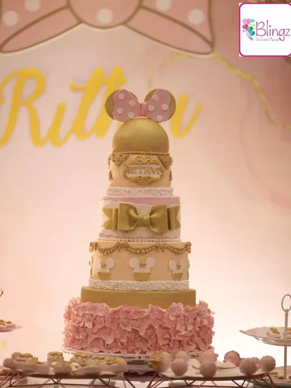 A close-up of a magnificent five-tiered Minnie Mouse cake. The design incorporates gold accents, delicate ruffles, and iconic bows, making it a true showstopper.