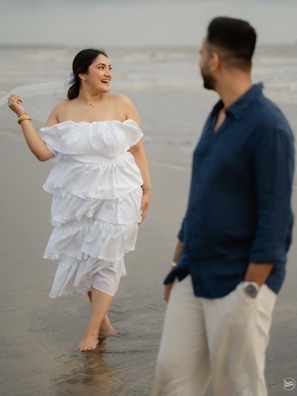 A candid moment of a woman walking on the beach in a beautiful white dress, with her partner looking on. This shot from their Alibaug pre-wedding session captures a sense of freedom and natural interaction.