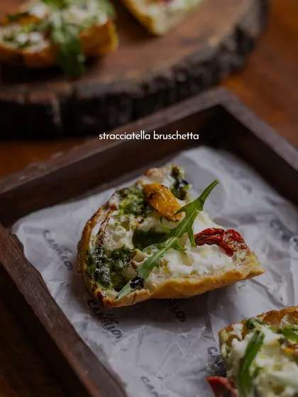 A close-up of the Stracciatella Bruschetta, showing the layers of creamy cheese, pesto, and fresh toppings on our house-made bread.