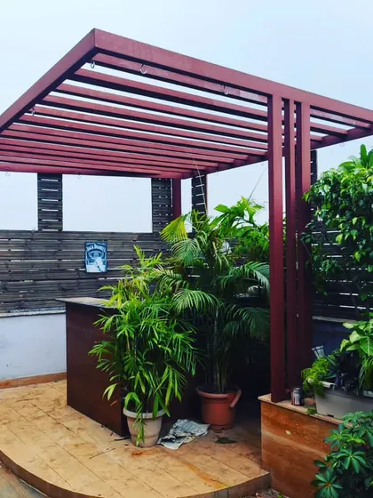 A rustic red pergola with a bar counter, surrounded by lush greenery. This structure adds a pop of color and a functional entertainment space to the terrace.