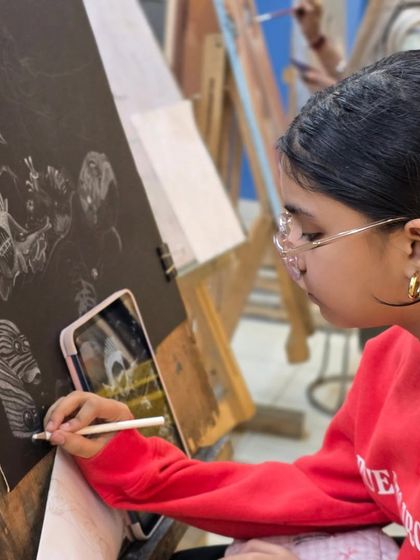 A student uses her phone as a reference while working on a detailed drawing with a glass marking pencil. Technology can be a great tool in the traditional art process.