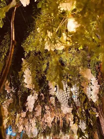 A close-up of the enchanted forest entrance tunnel. The ceiling is a dense mix of green foliage, white flowers, and hanging crystal chandeliers, creating a lush and magical effect.