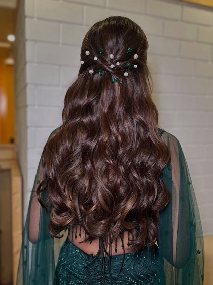 A half-updo with a twist, adorned with green and white pearl pins. This is a great way to add a touch of color and elegance to a simple wavy hairstyle.