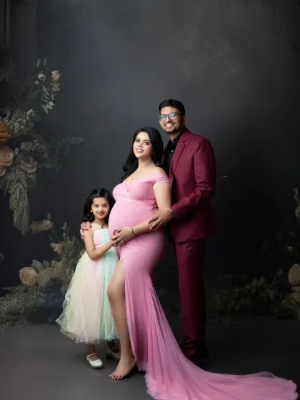 An elegant family maternity portrait against a moody, dark backdrop. The family's coordinated outfits in shades of pink and burgundy create a sophisticated and cohesive look.